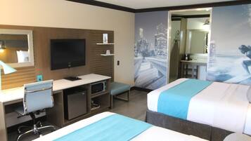 A hotel room with two beds, a desk with a computer, a TV, and a bathroom visible through an open door.