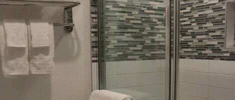 A modern bathroom with a glass-enclosed shower, a toilet, and a towel rack with folded towels.