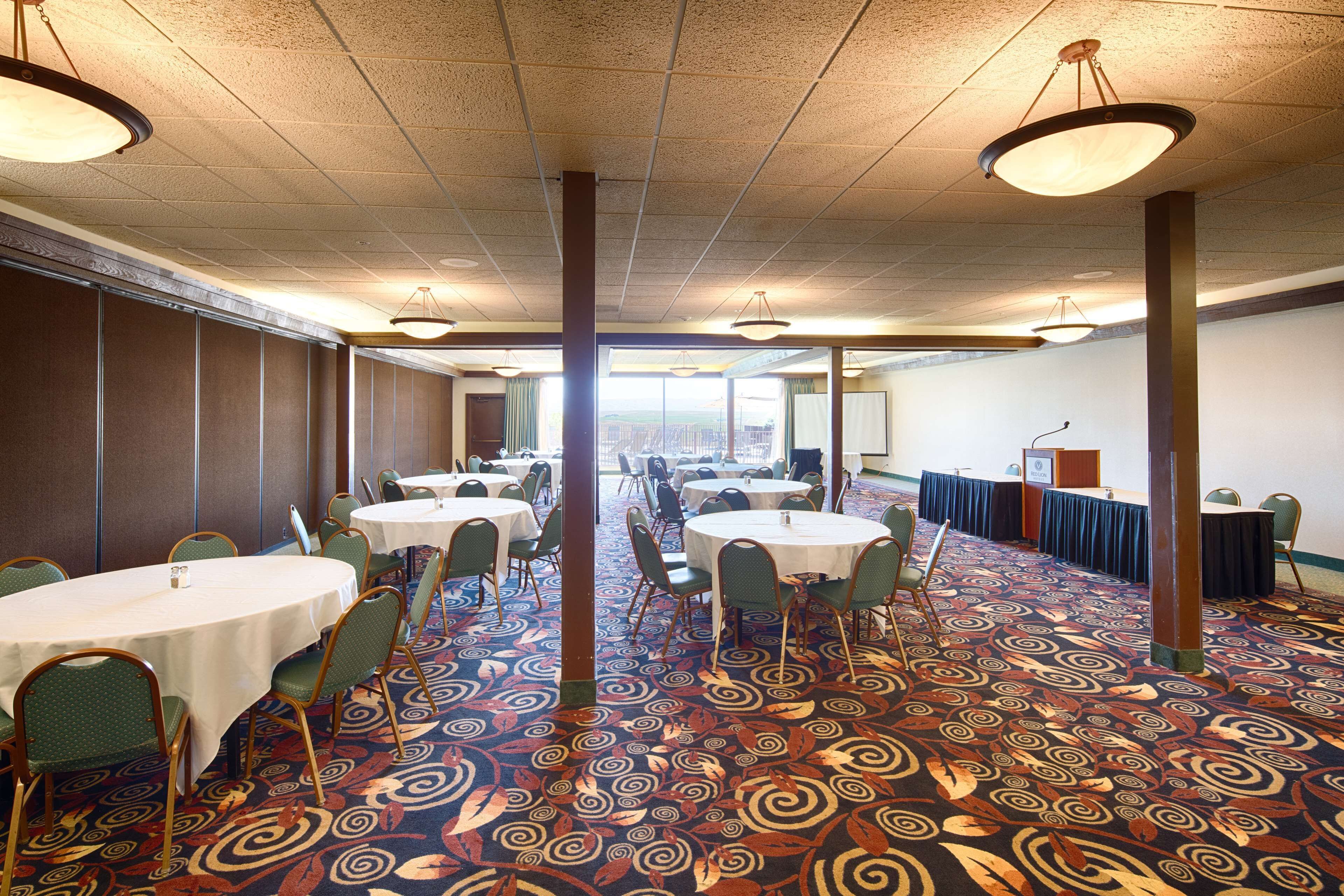 A conference room with round tables, green chairs, and a patterned carpet.