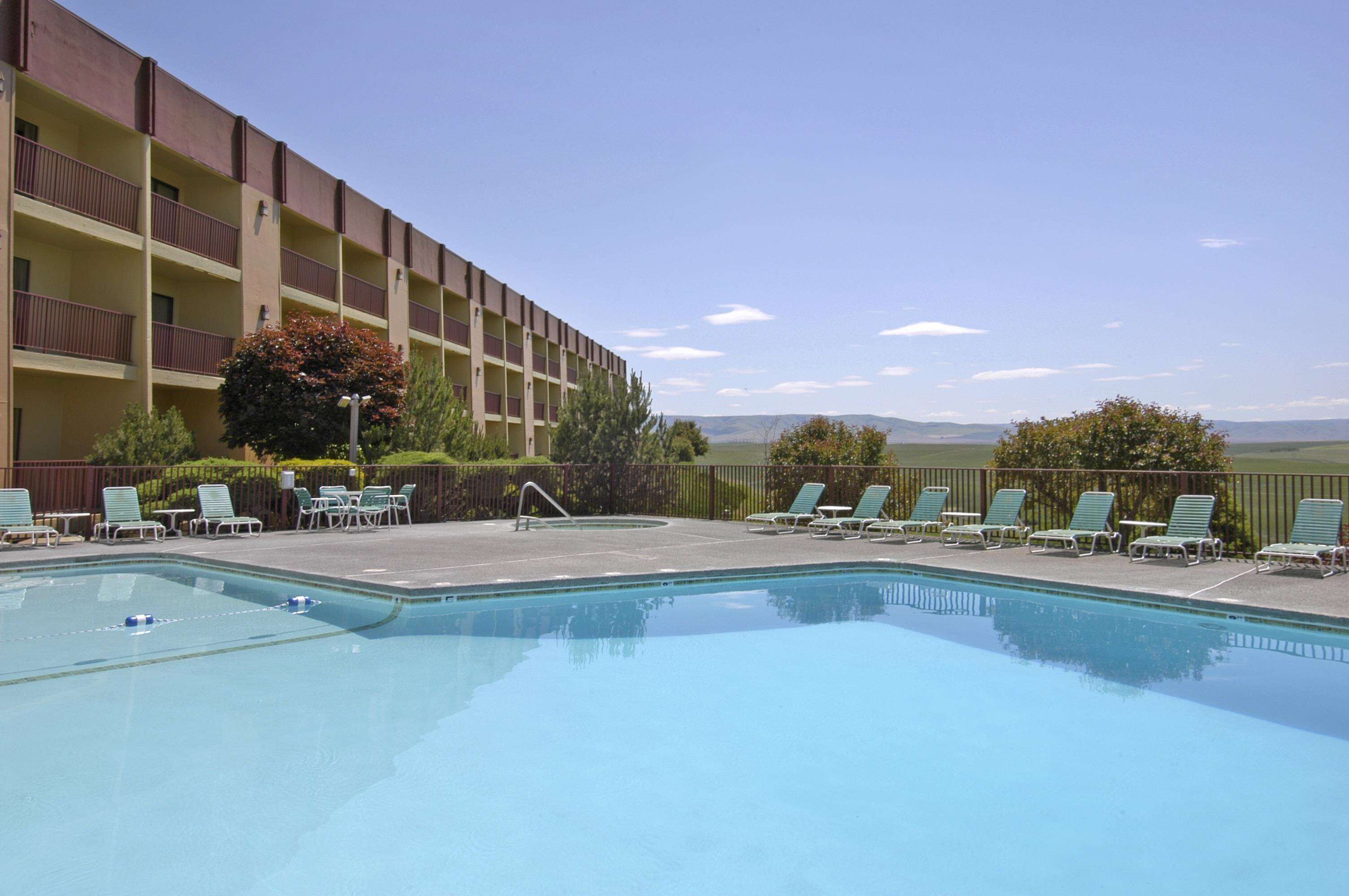 Una piscina con sillas de descanso, un edificio con balcones y vistas a montañas distantes.