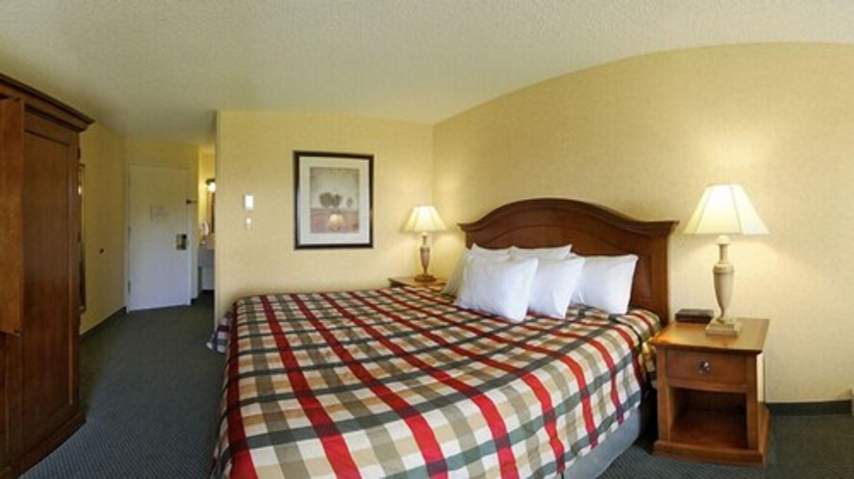 Una habitación de hotel con una cama grande, dos mesitas de noche con lámparas, un armario de madera y un cuadro enmarcado en la pared.