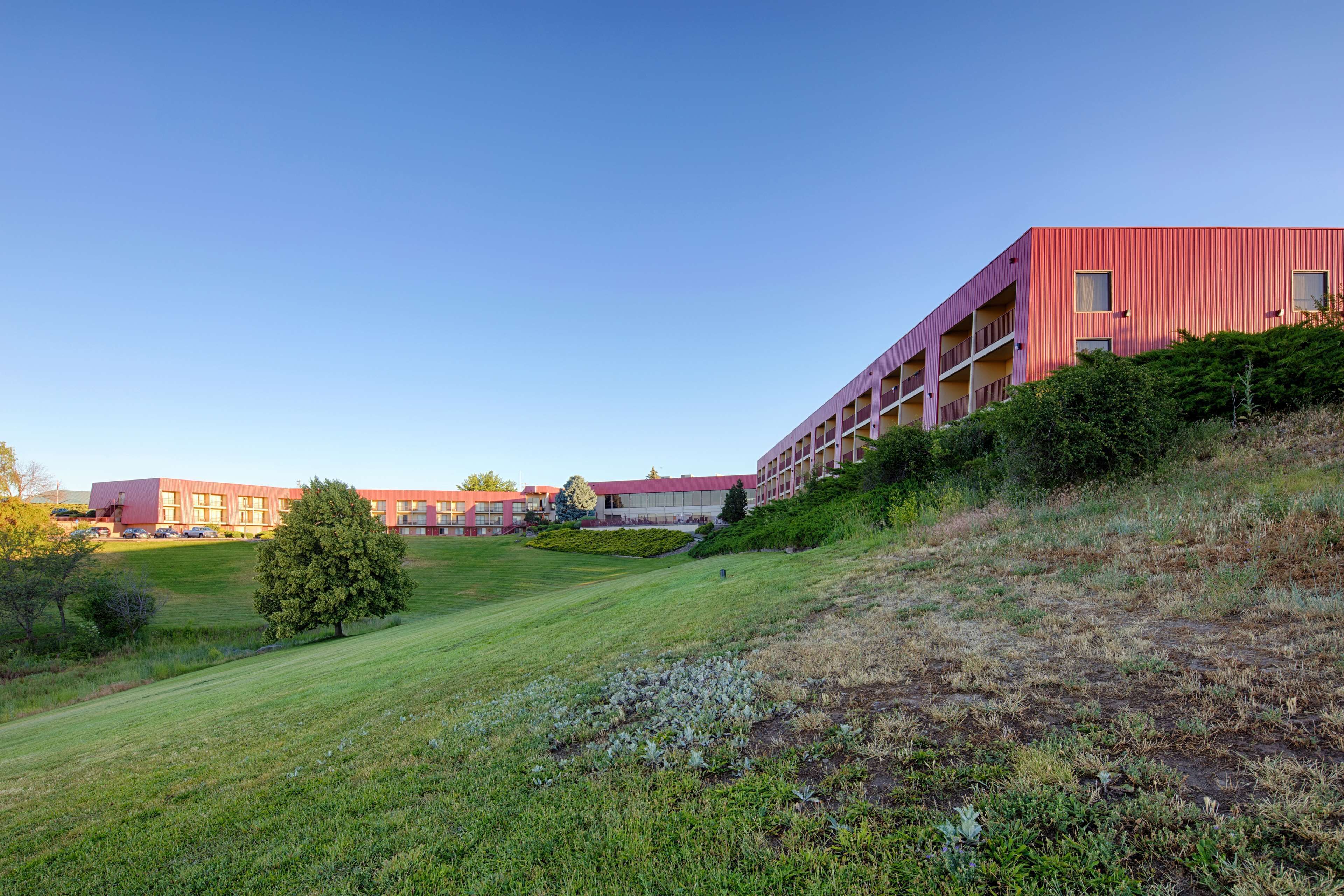 A modern building with a red facade, multiple balconies, and a grassy area in front.