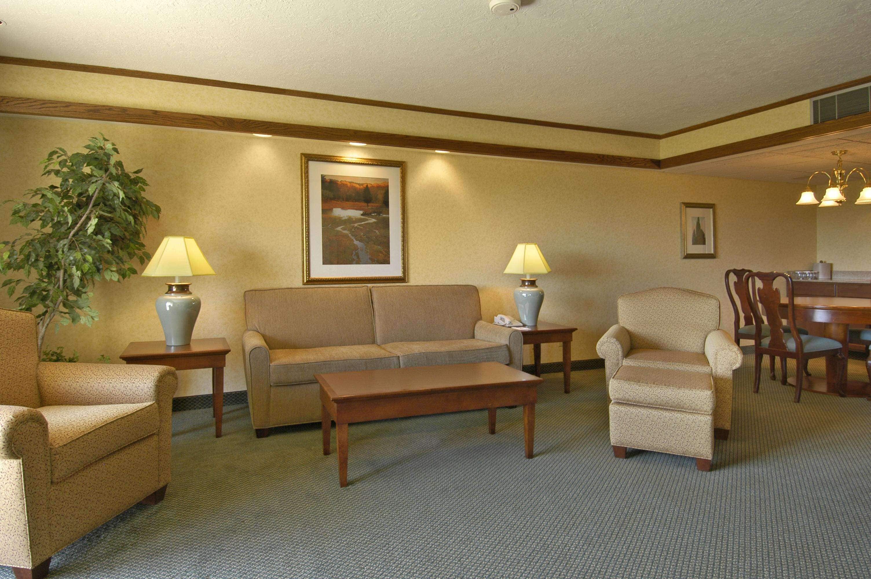 A hotel room with a sofa, armchairs, a coffee table, a dining table with chairs, a lamp, and a framed picture on the wall.