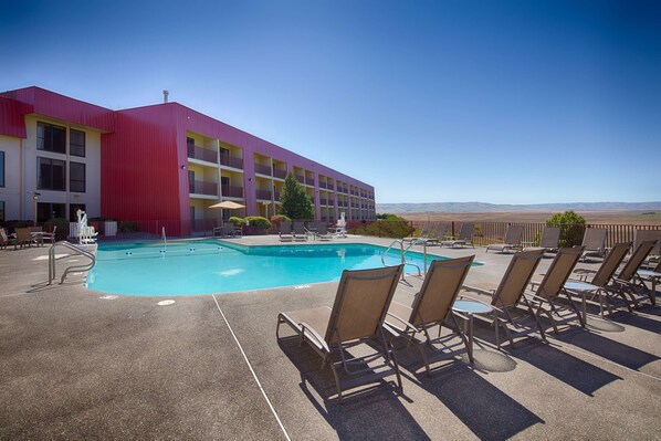 A hotel with a swimming pool, lounge chairs, and a view of the mountains.
