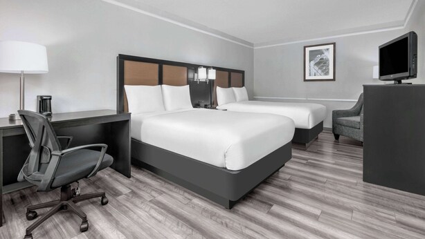 Une chambre d’hôtel avec deux lits, un bureau, une chaise, une télévision et une lampe.