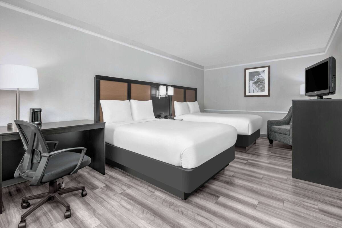 A hotel room with two beds, a desk, a chair, a television, and a lamp.
