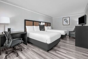 Habitación de hotel con dos camas, un escritorio, una silla, un televisor y una lámpara.