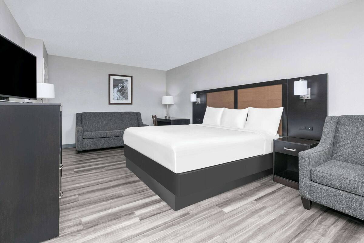 A modern hotel room with a large bed, a desk, a chair, and a television.