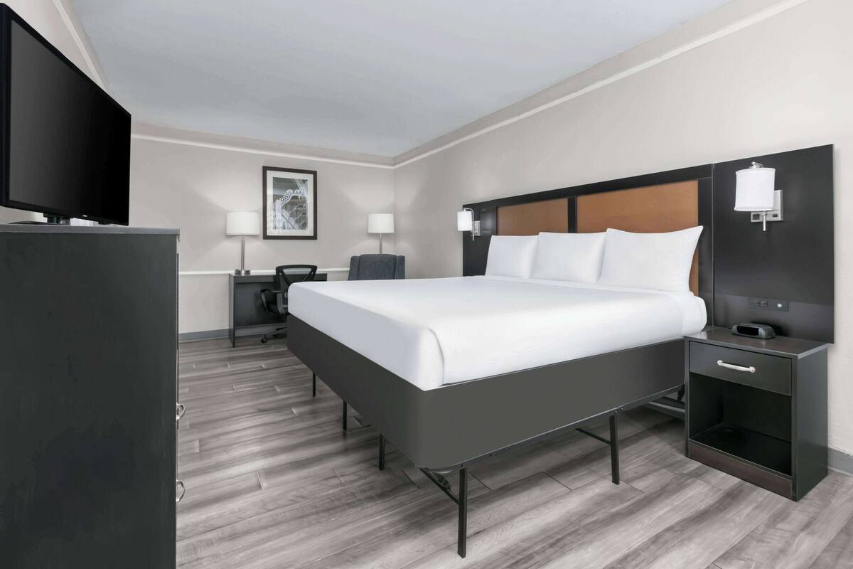 A modern hotel room with a large bed, a flat-screen TV, a desk, and a chair.