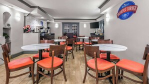 Un coin petit-déjeuner avec des chaises et des tables en bois, un espace cuisine et un panneau accroché au mur.