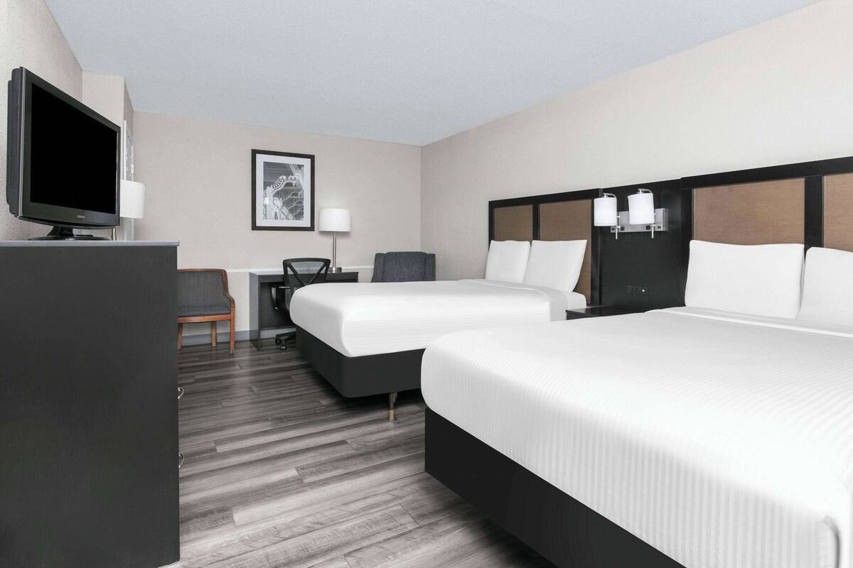 A hotel room with two beds, a desk with a chair, a television, and a framed picture on the wall.