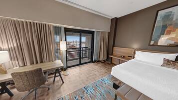 Ein Hotelzimmer mit Bett, Schreibtisch, Stuhl und Blick durch eine Schiebetür.