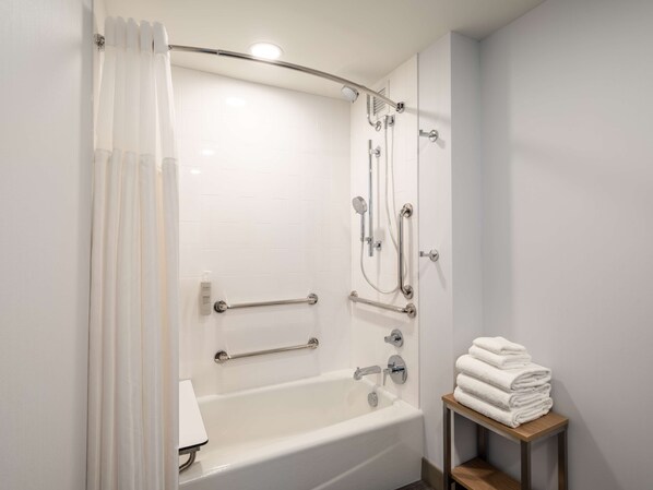 A modern bathroom with a walk-in shower, grab bars, a bathtub, and a stack of towels on a wooden table.