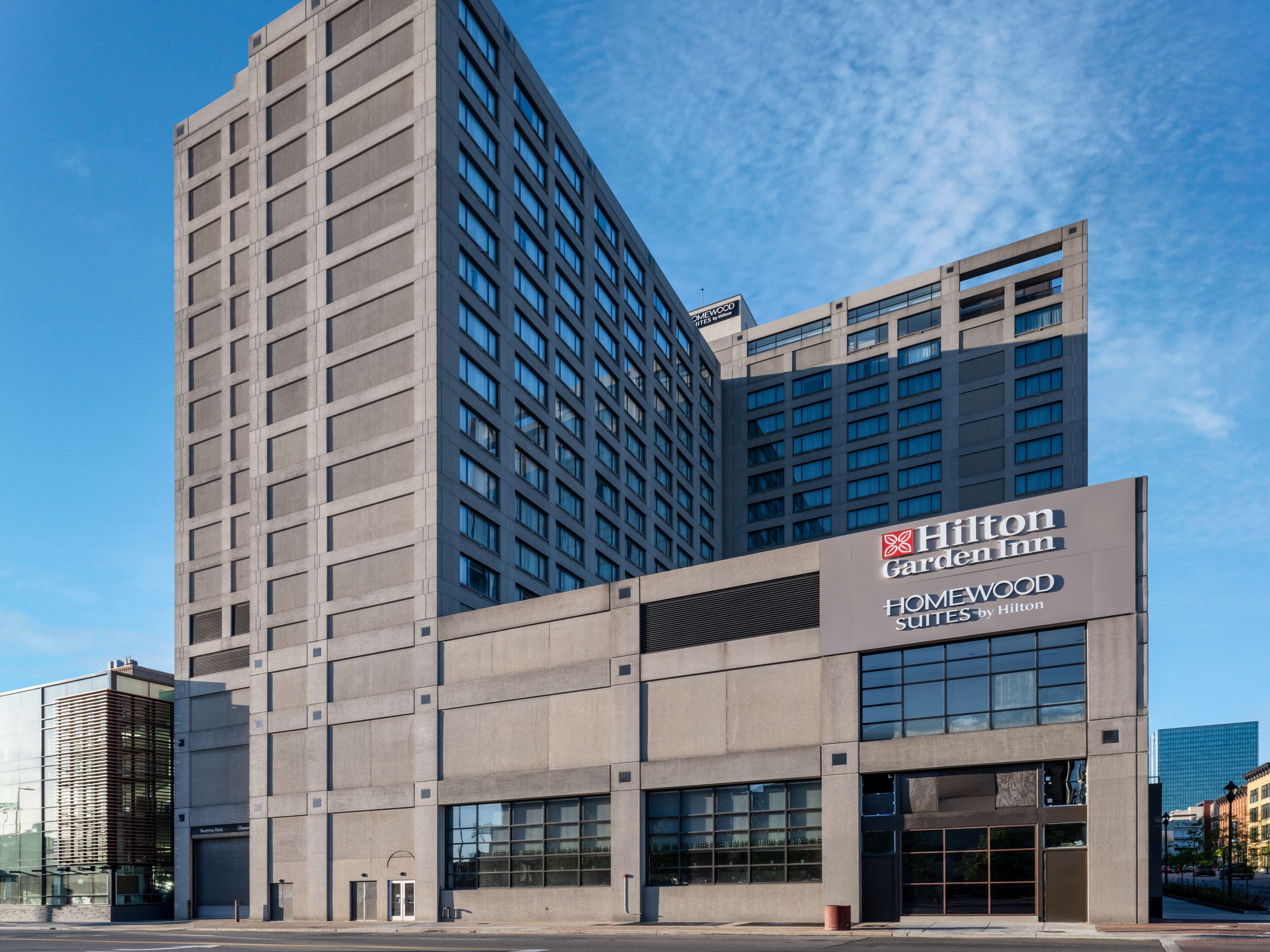 Um edifício moderno de hotel com uma placa Hilton Garden Inn em destaque, apresentando um design limpo e contemporâneo, com grandes janelas e fachada estruturada.
