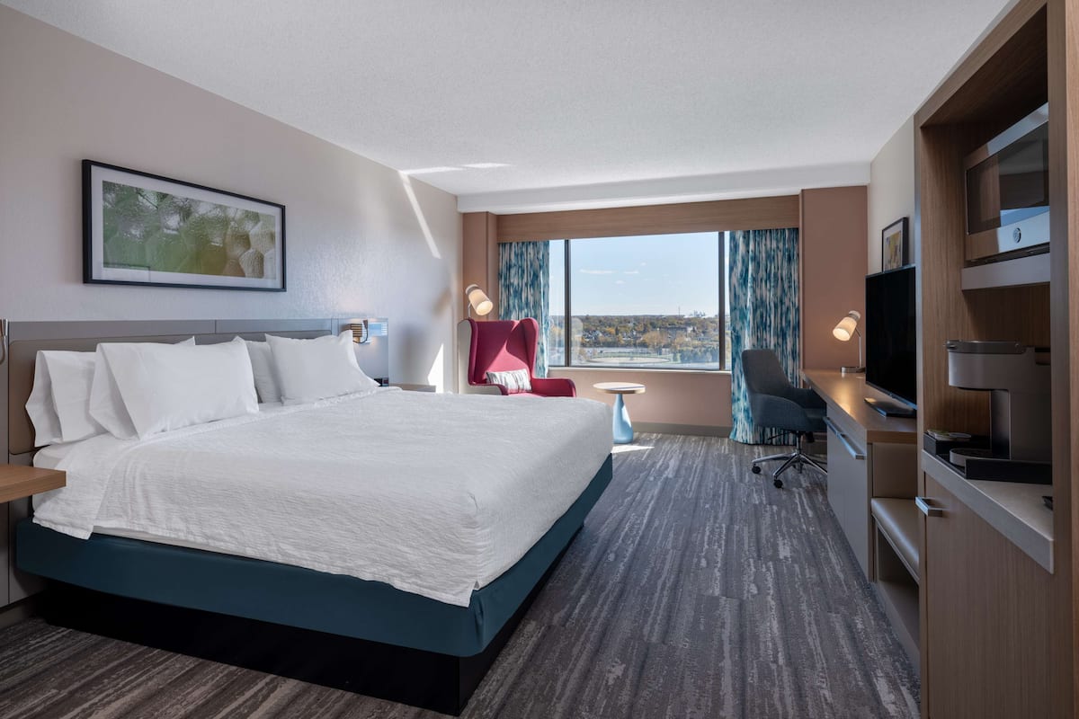 A hotel room with a large bed, a desk with a computer, a TV, and a window with a city view.
