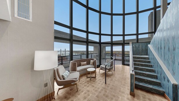A spacious living area with a curved glass wall, a sofa, a chair, and a small table. - Hilton Garden Inn Toledo Downtown (Toledo)