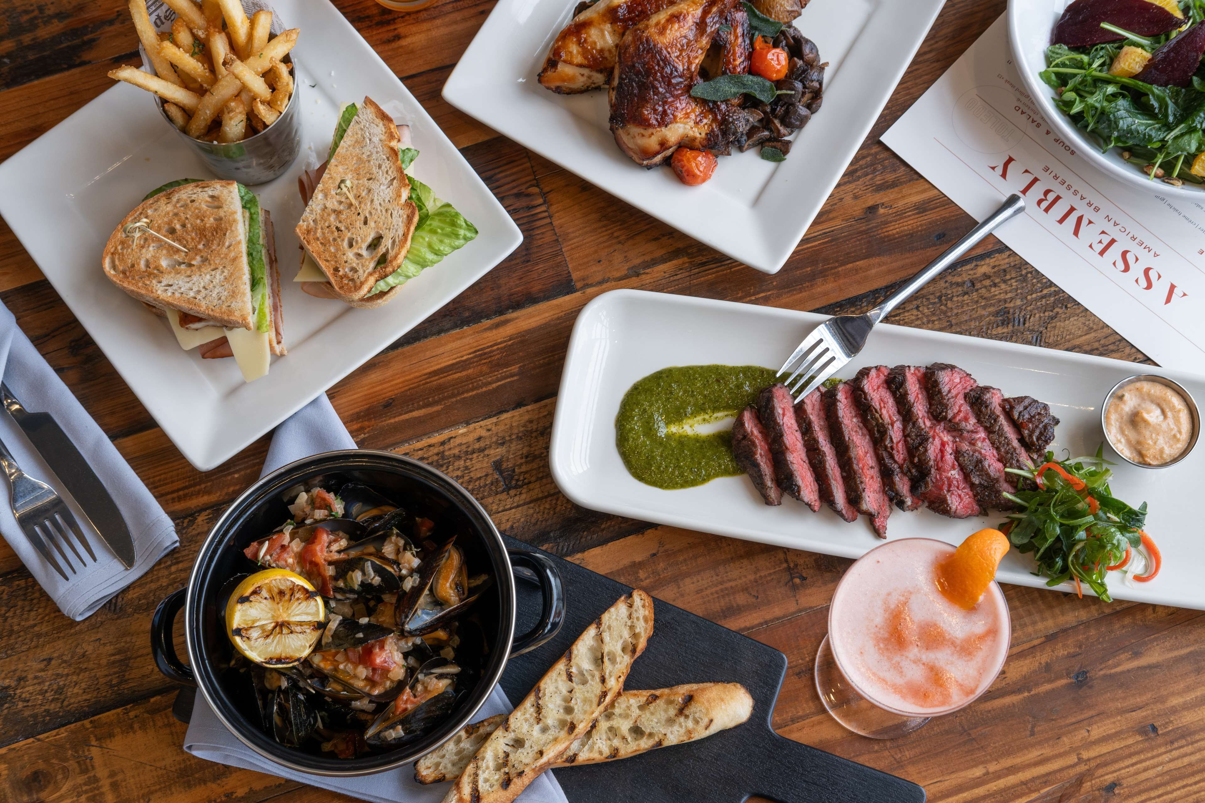 A variety of dishes including a sandwich, steak, fries, and a salad on a wooden table.