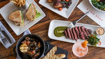 A variety of dishes including a sandwich, steak, fries, and a salad on a wooden table.
