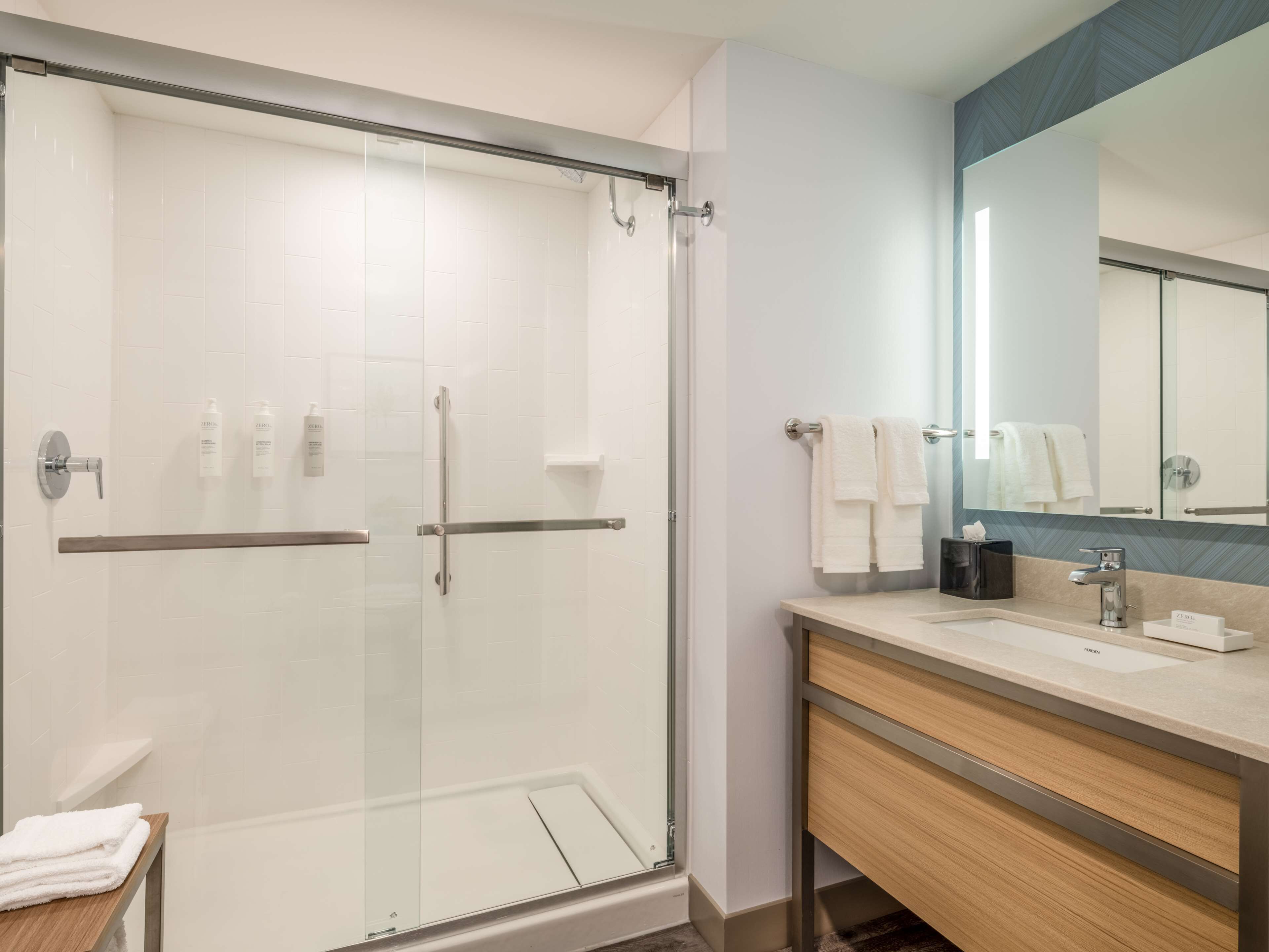 A modern bathroom with a glass shower enclosure, a wooden vanity, and a large mirror.