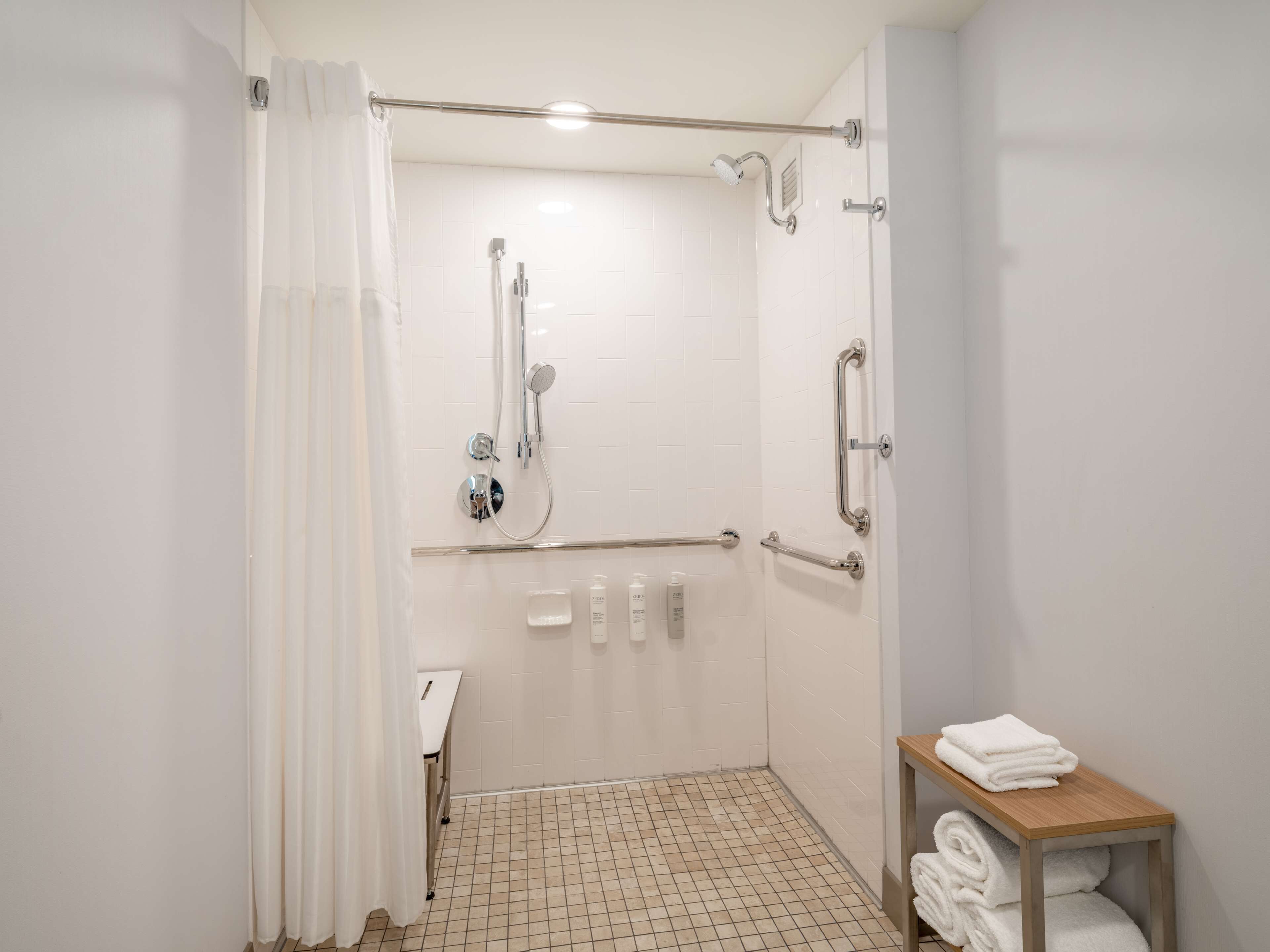 Une salle de bain moderne dotée d’une douche à l’italienne, de barres d’appui, d’un petit lavabo et d’un porte-serviettes.