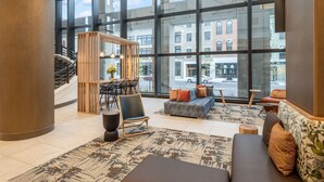A spacious lobby with a large window, a staircase, a seating area with a sofa and chairs, and a small table with a vase of flowers. - Hilton Garden Inn Toledo Downtown (Toledo)