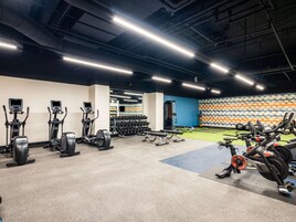Un gimnasio con diversos equipos de ejercicio, que incluye cintas de correr, máquinas elípticas y zonas de levantamiento de pesas.