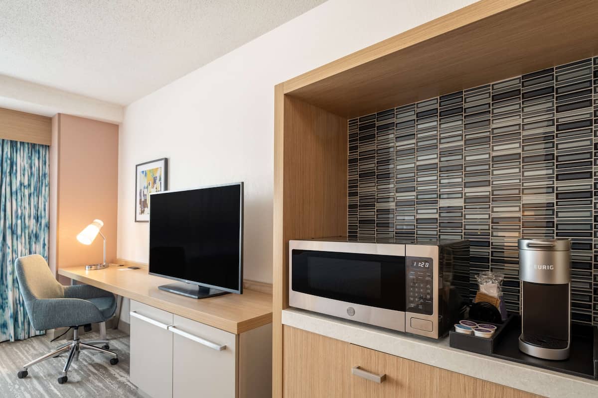A modern hotel room with a wooden desk, a flat-screen TV, a built-in microwave, and a coffee maker.