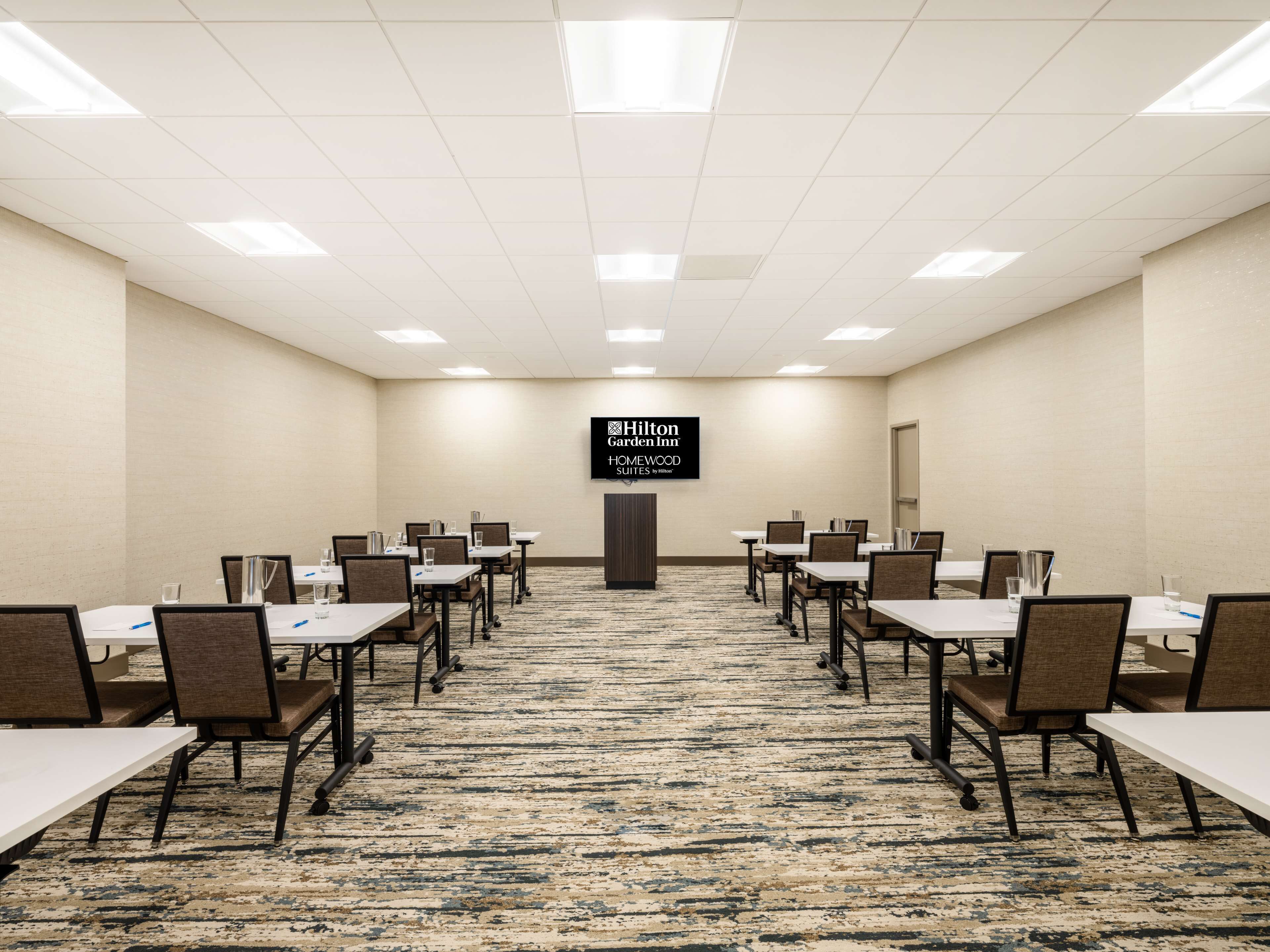 Un salón de conferencias con mesas y sillas, suelo alfombrado y un cartel de Hilton Garden Inn.