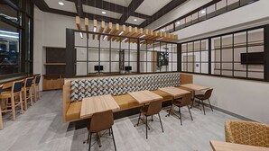 A modern dining area with wooden tables and chairs, a patterned bench, and a large window with a view. - Hilton Garden Inn Toledo Downtown (Toledo)