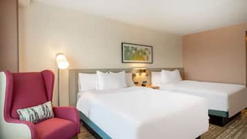 Habitación de hotel con dos camas, un sillón rojo, una mesita y una lámpara de pared.
