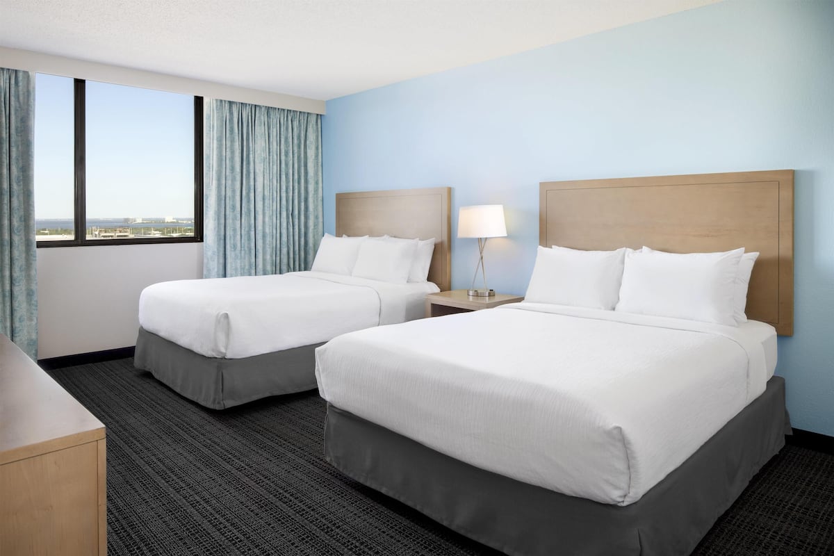 Ein Hotelzimmer mit zwei Betten, Blick auf die Stadt und einem großen Fenster mit Vorhängen.