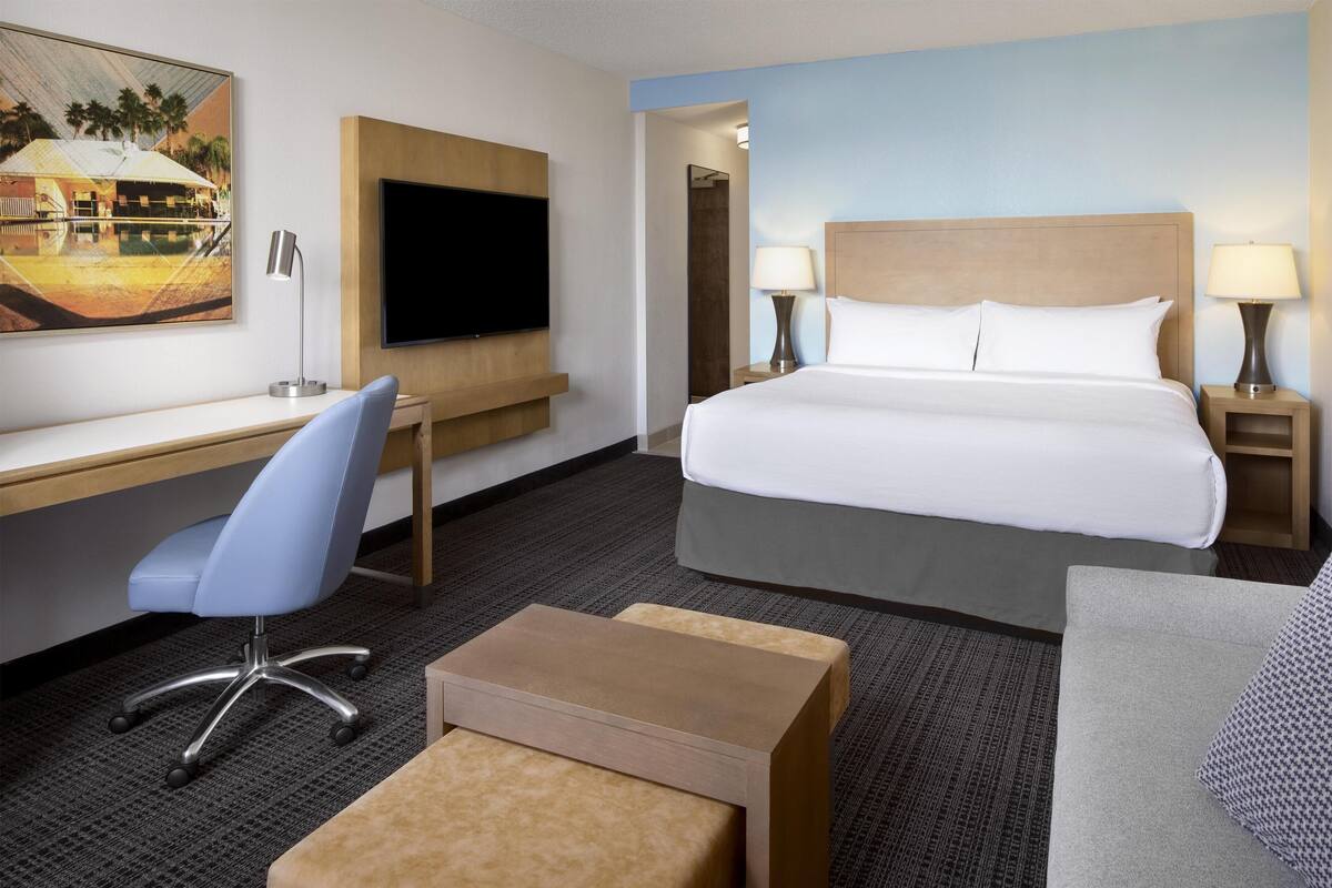 A hotel room with a large bed, a desk with a chair, a TV, and two bedside lamps.