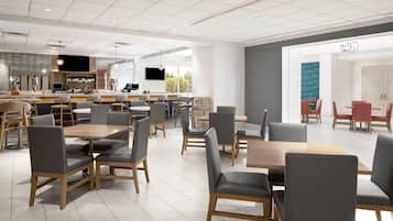 A modern cafe with multiple seating areas, a bar, and a large window providing natural light.