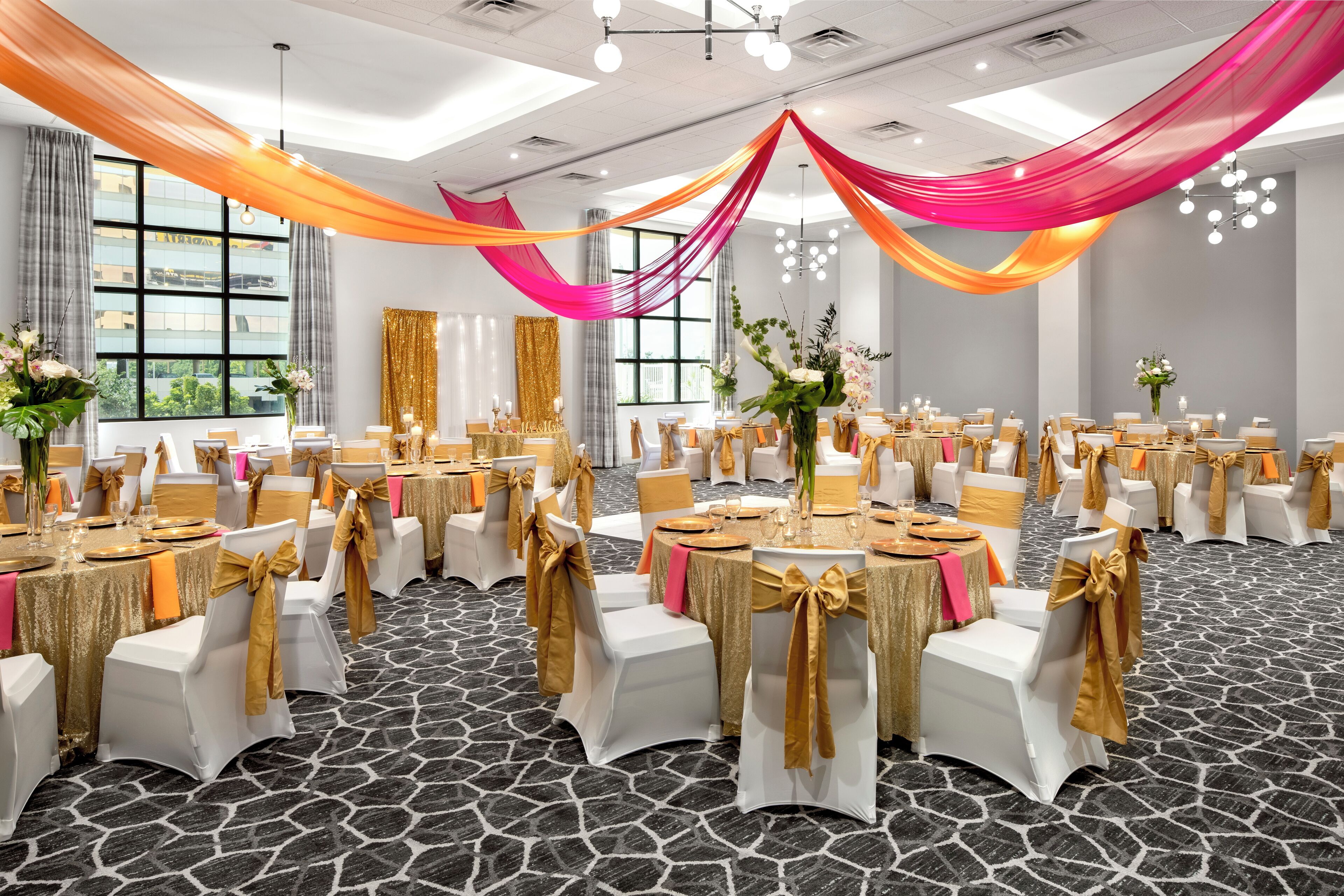 Une salle de banquet avec des tables rondes, des chaises blanches et des rubans dorés.