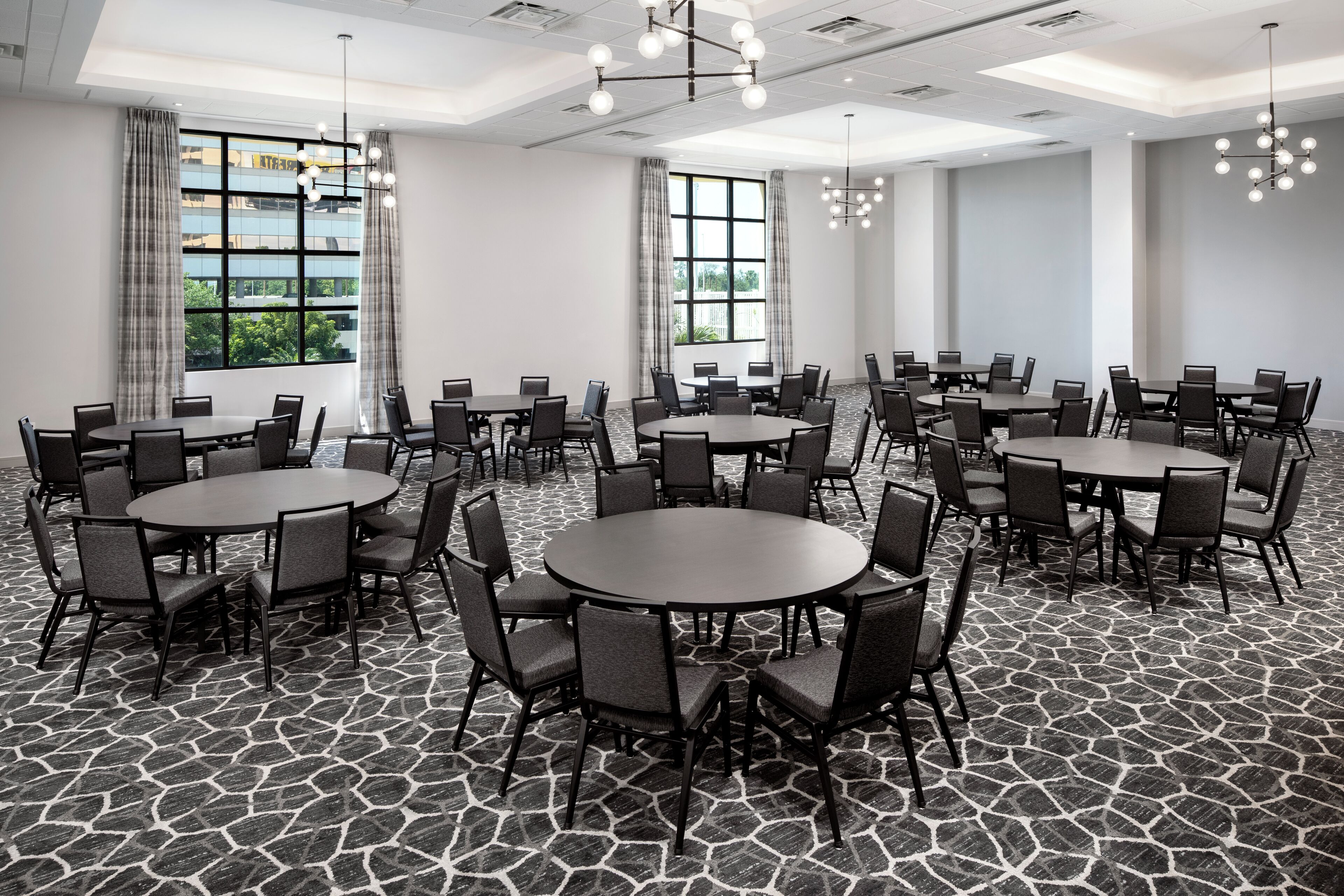 A conference room with multiple tables and chairs, large windows with curtains, and a patterned floor.