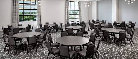 A conference room with multiple tables and chairs, large windows with curtains, and a patterned floor.