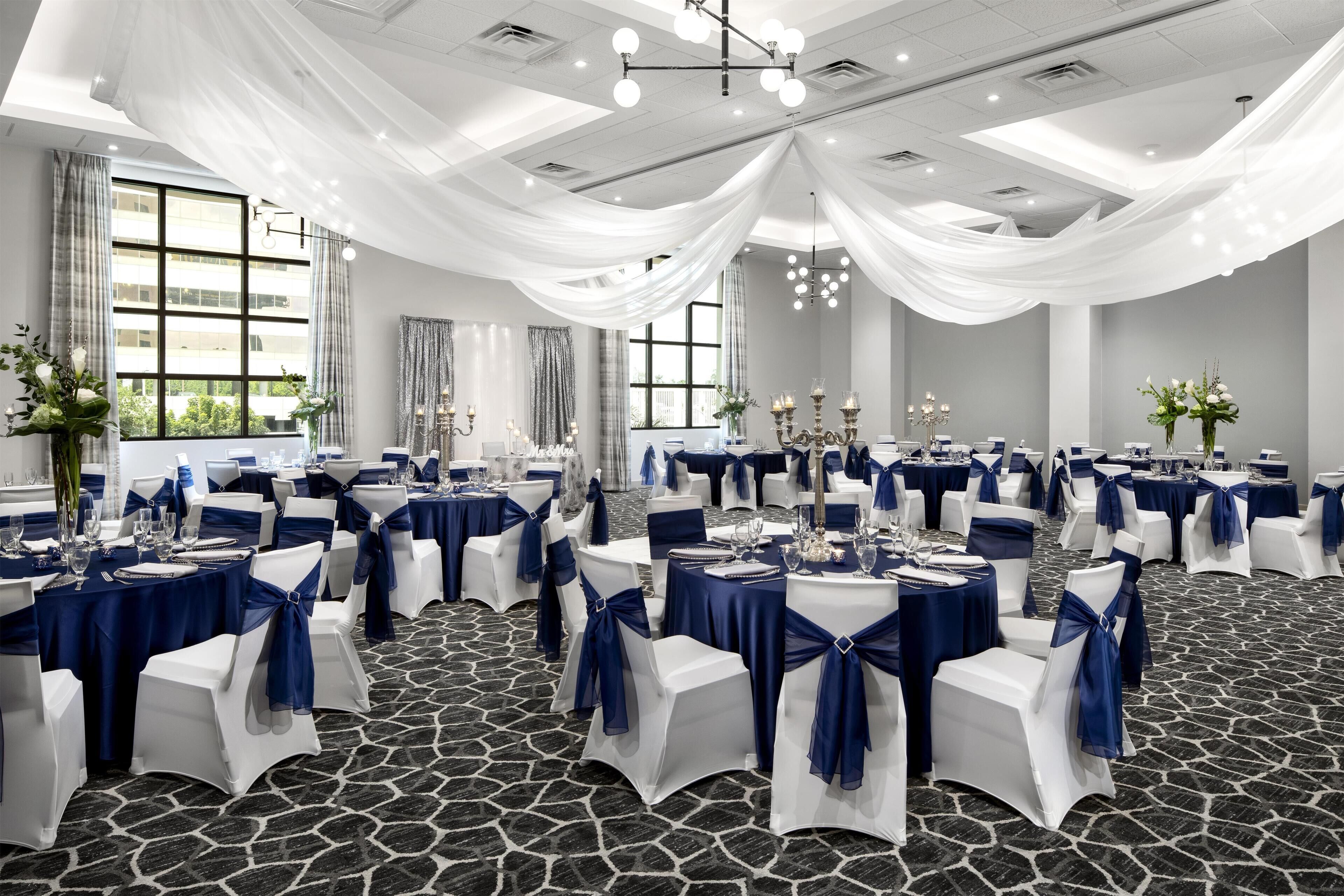 A banquet hall with round tables, white chairs, and blue drapes.