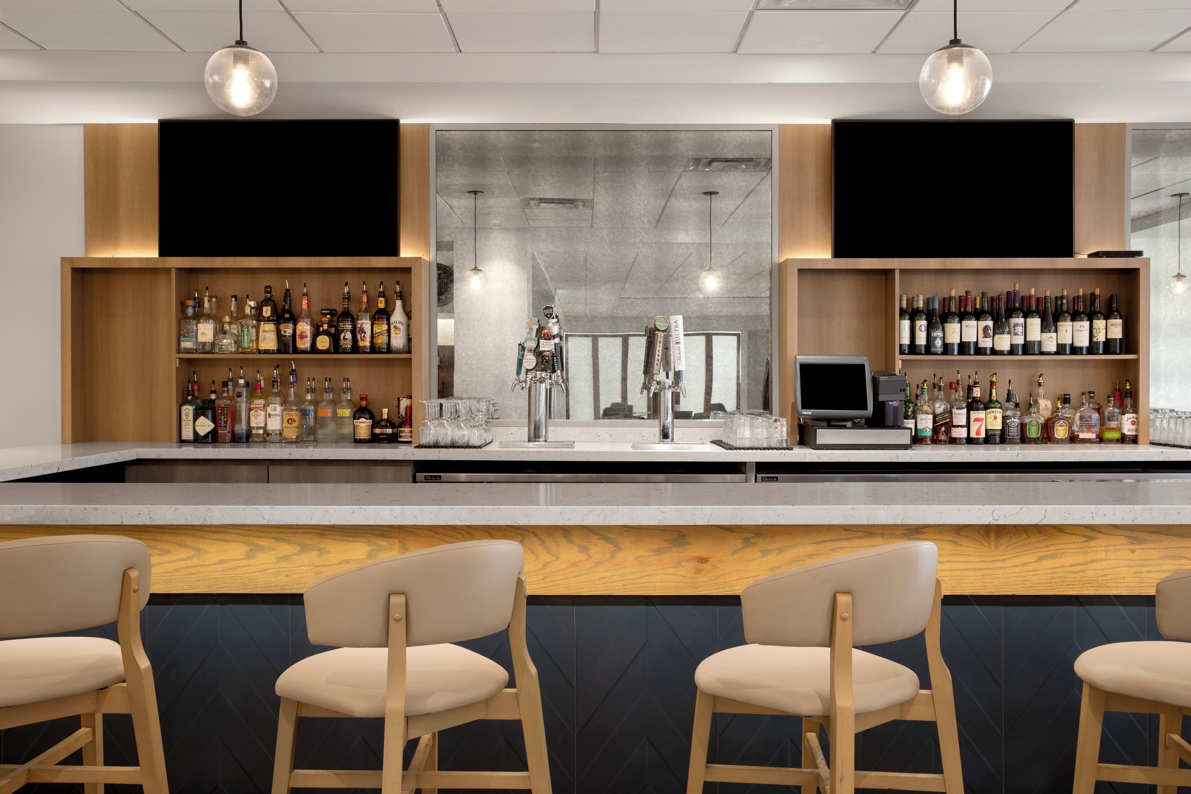 Un espace bar avec des étagères en bois remplies de bouteilles, un comptoir et deux tabourets de bar.