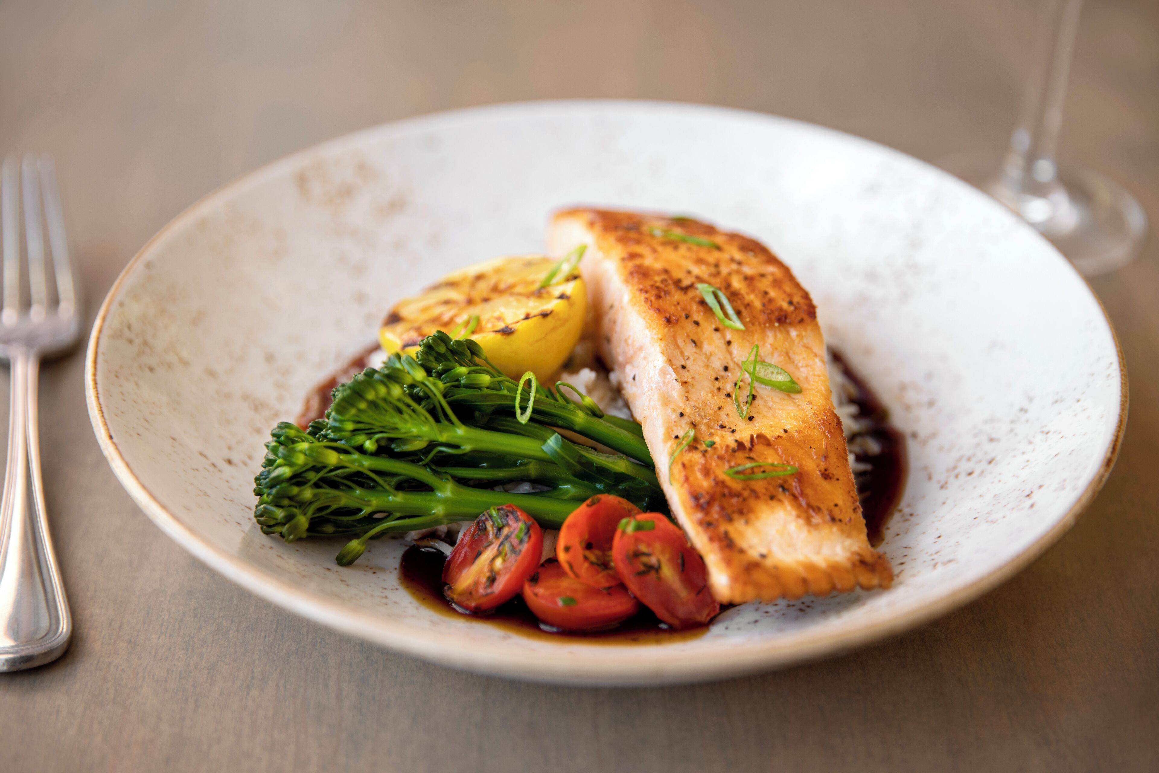 A plate with grilled fish, broccoli, and cherry tomatoes.