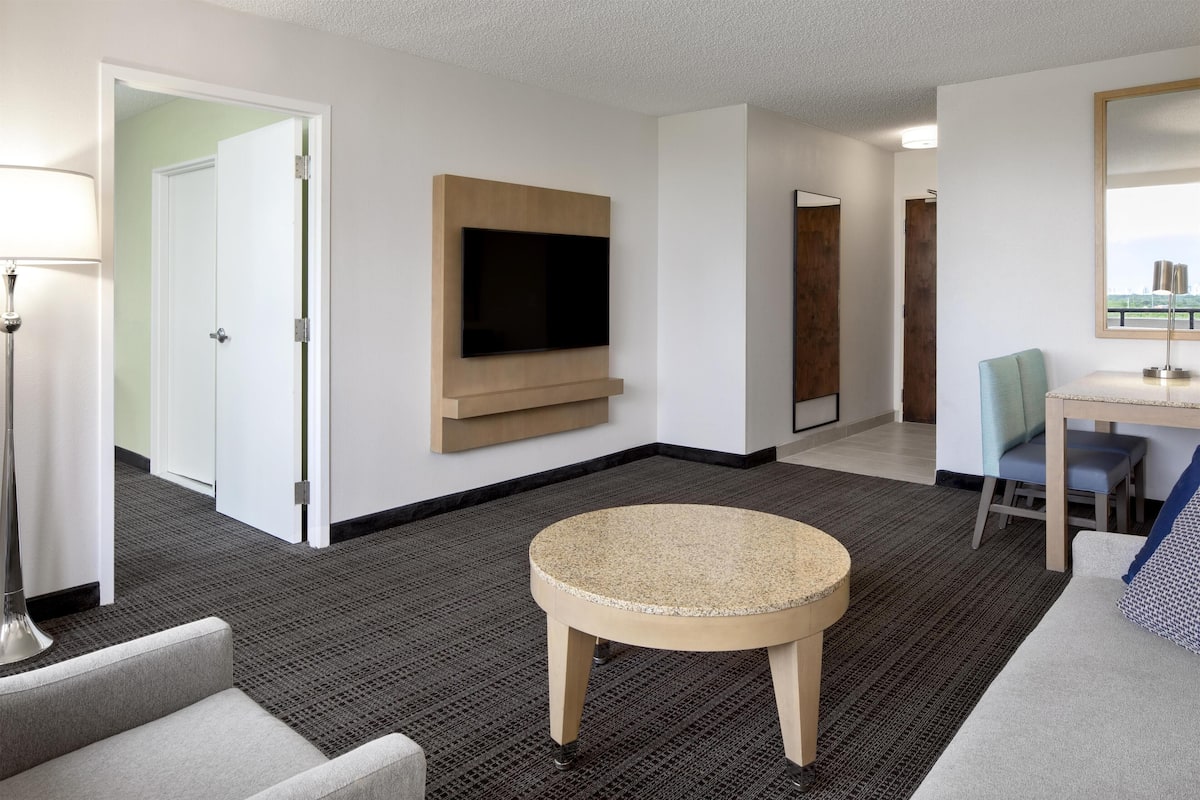 Ein Hotelzimmer mit Flachbildfernseher an der Wand, einem runden Tisch, einer Couch und einem Schreibtisch mit Stuhl.