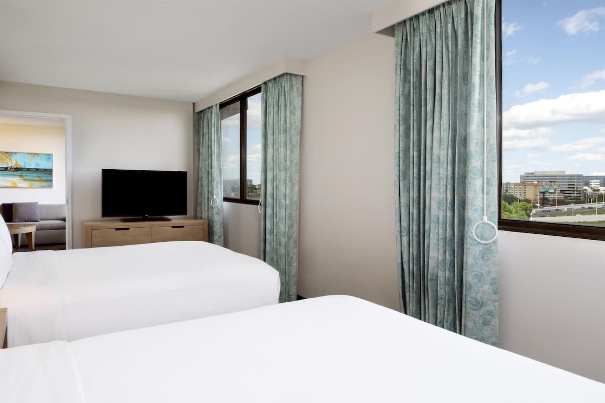 Ein Hotelzimmer mit zwei Betten, einem Fernseher, einem Gemälde und einem Fenster mit Vorhängen.