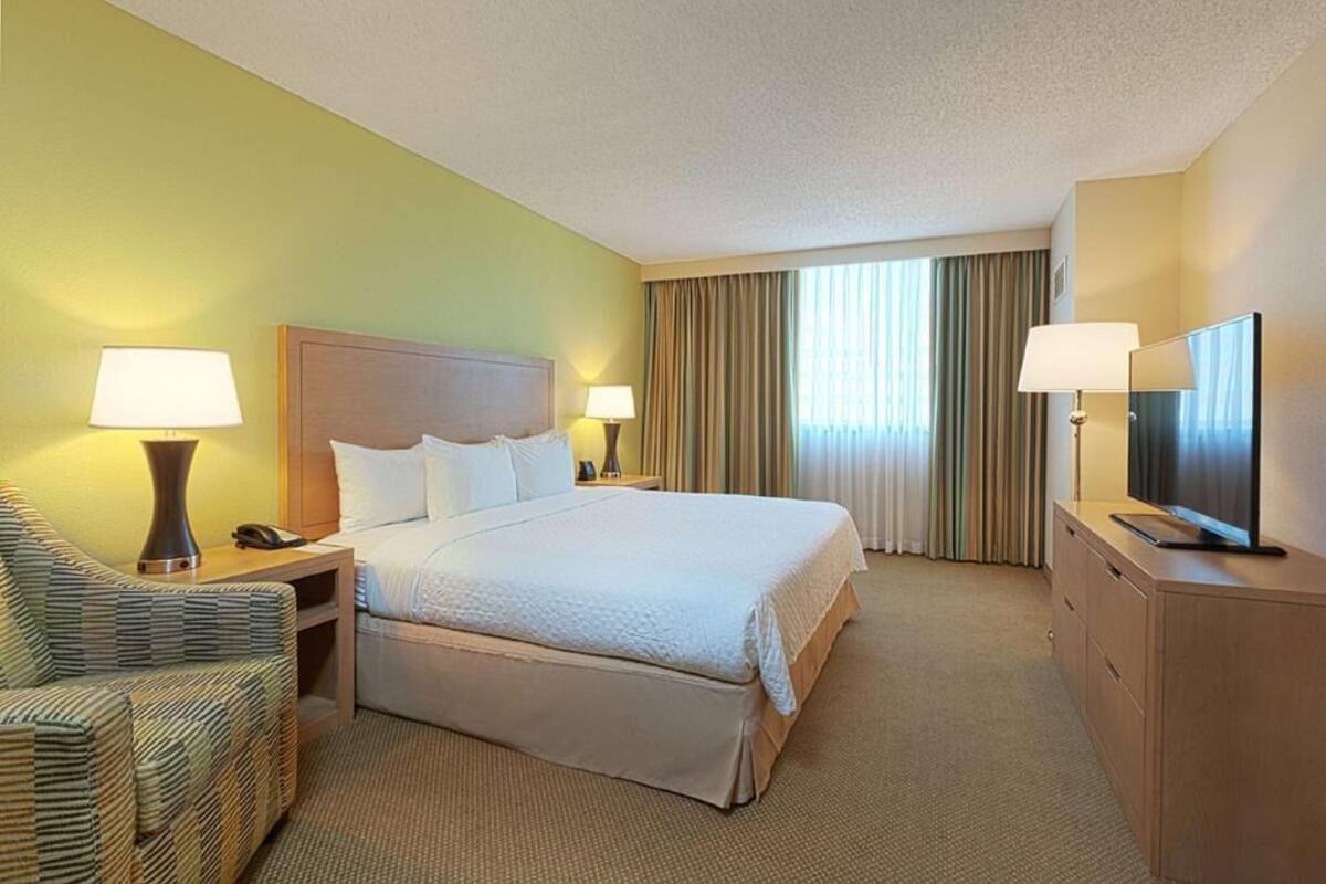A hotel room with a bed, a chair, a desk, a television, and a window with curtains.