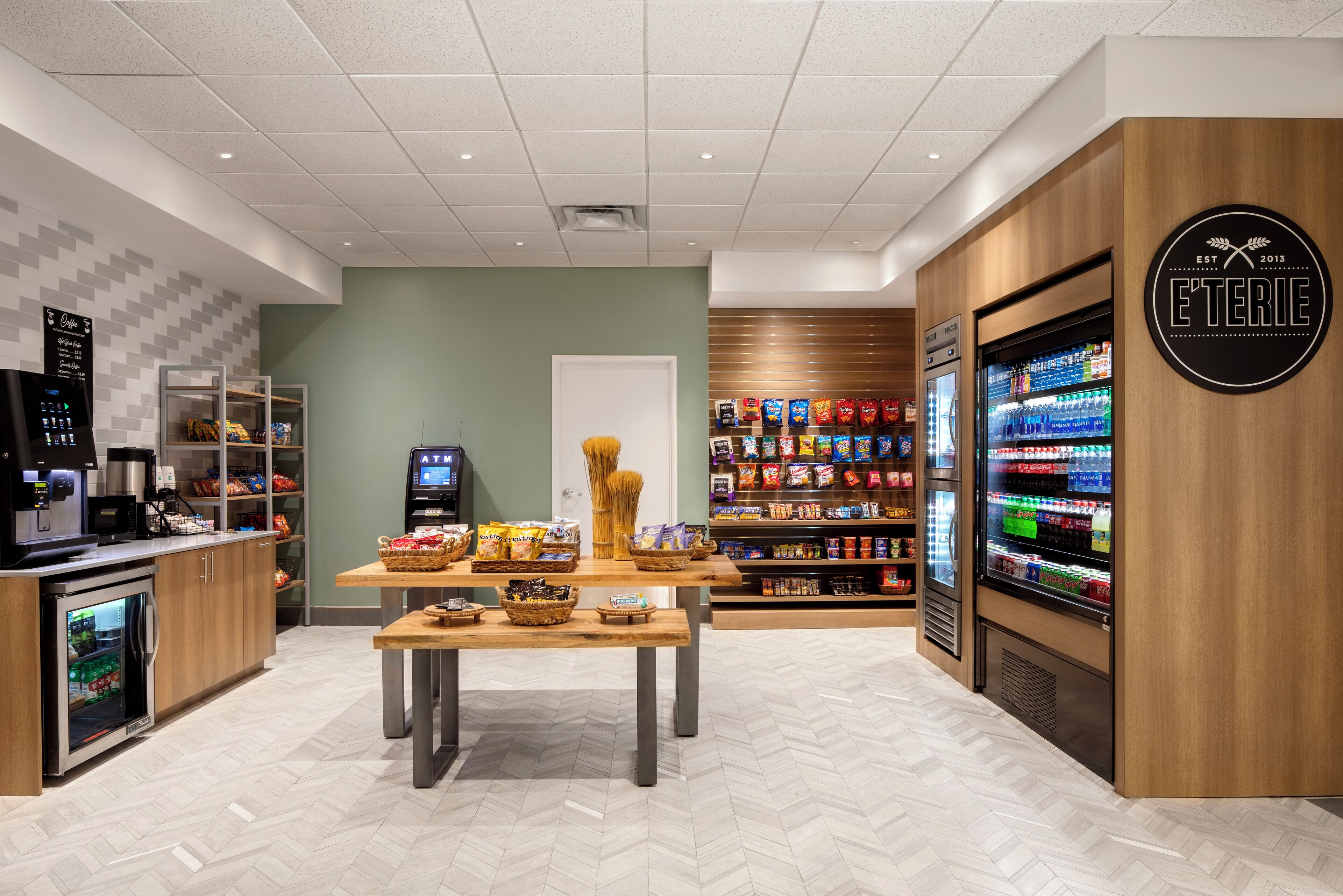 A modern food service area with a coffee machine, snack display, and a refrigerated beverage dispenser.