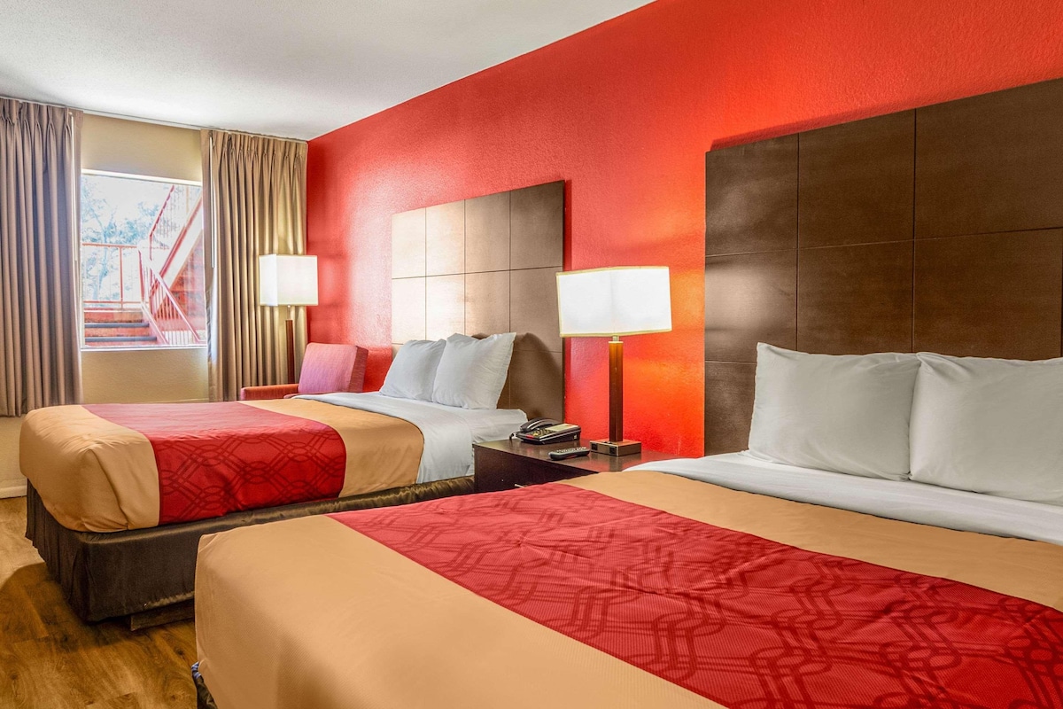 A hotel room with two beds, a large window with curtains, and a view of a red staircase outside.
