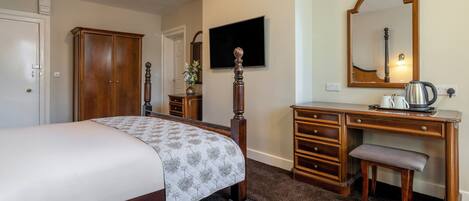 A bedroom with a bed, a wooden dresser, a desk with a mirror, and a television.
