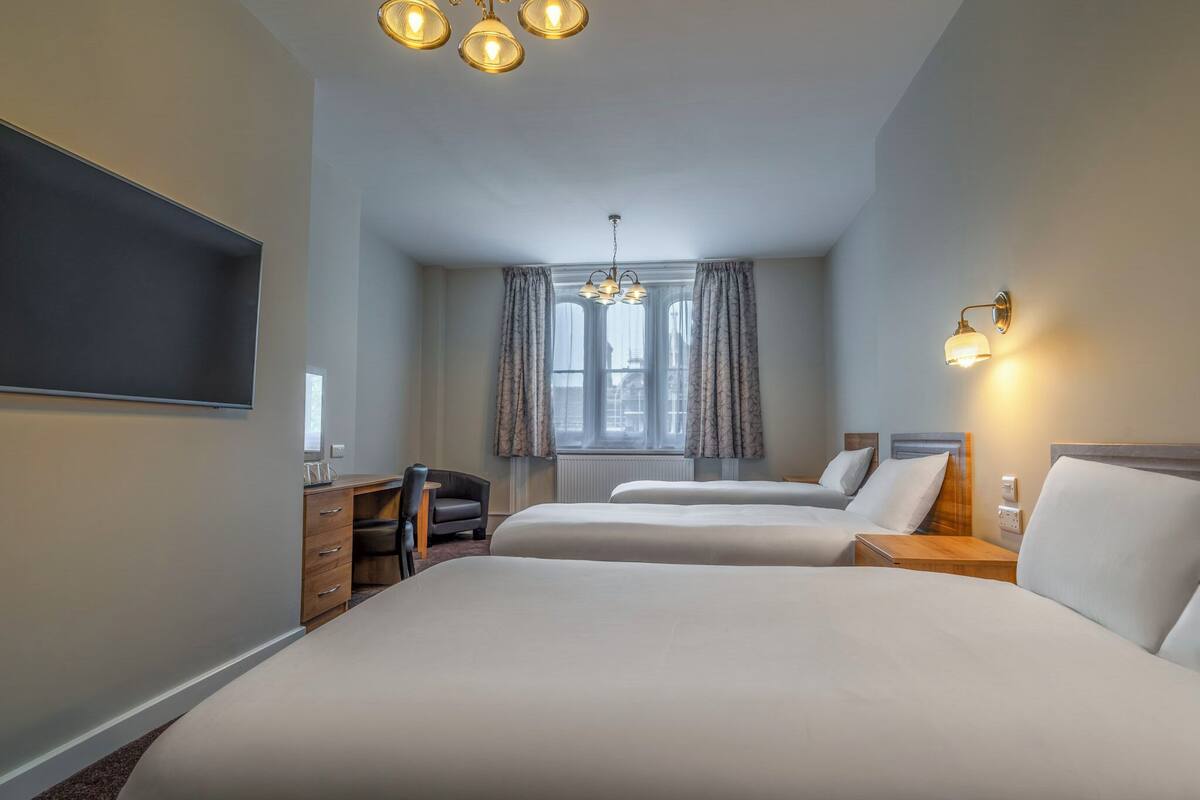 A hotel room with two beds, a desk, a chair, a TV, and a window with curtains.