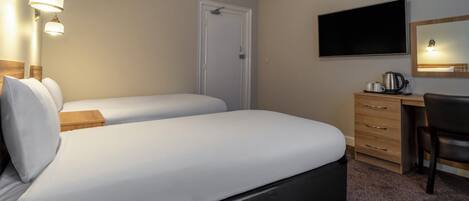 Habitación de hotel con dos camas, un escritorio, una silla, un televisor de pantalla plana y una cafetera.