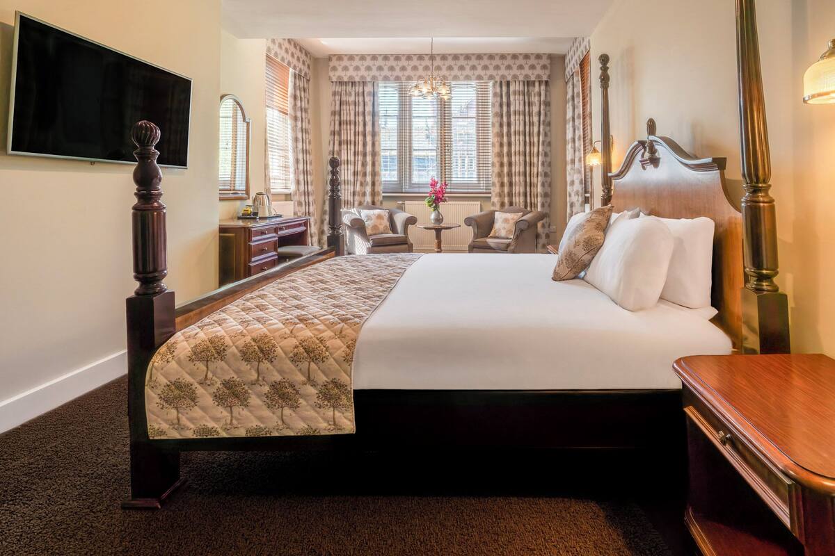 A hotel room with a large bed, a TV, a desk, and a chair.