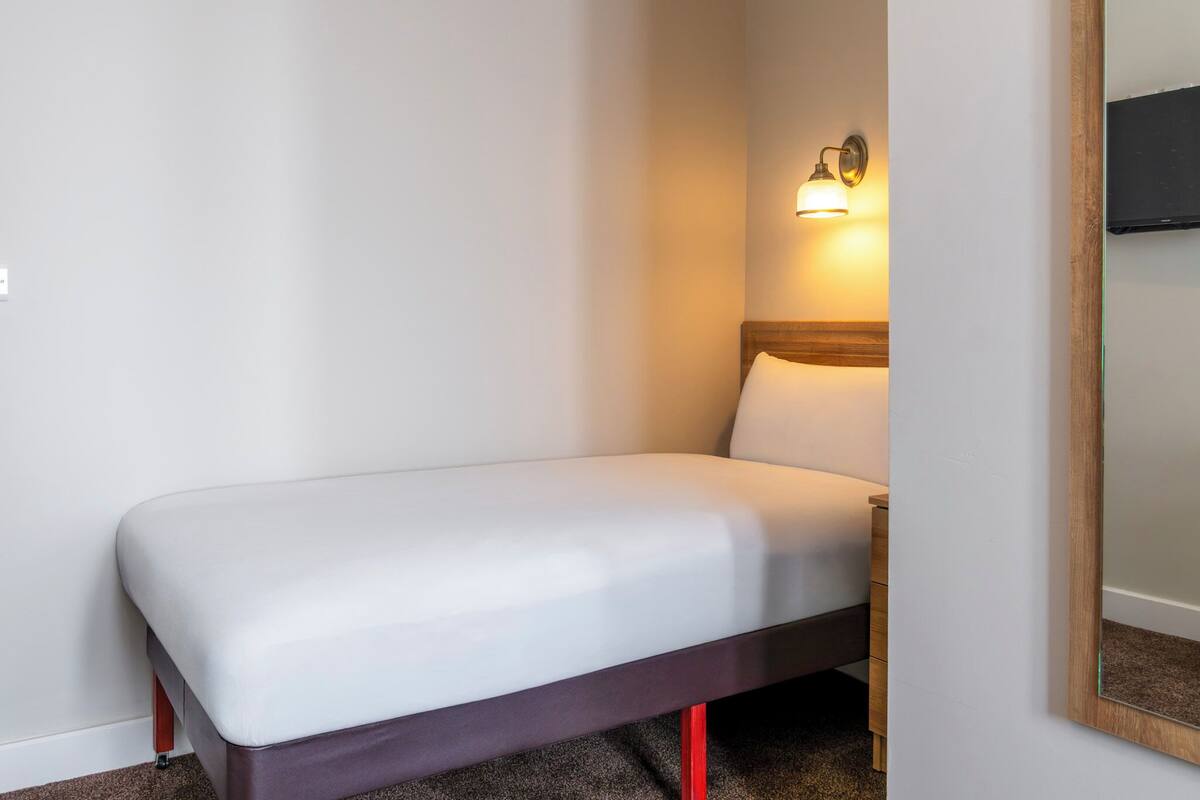 A single bed with a wooden headboard, a bedside table, and a wall-mounted light fixture.