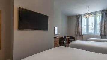 Habitación de hotel con dos camas, un escritorio con silla, un televisor de pantalla plana y una ventana con cortinas.